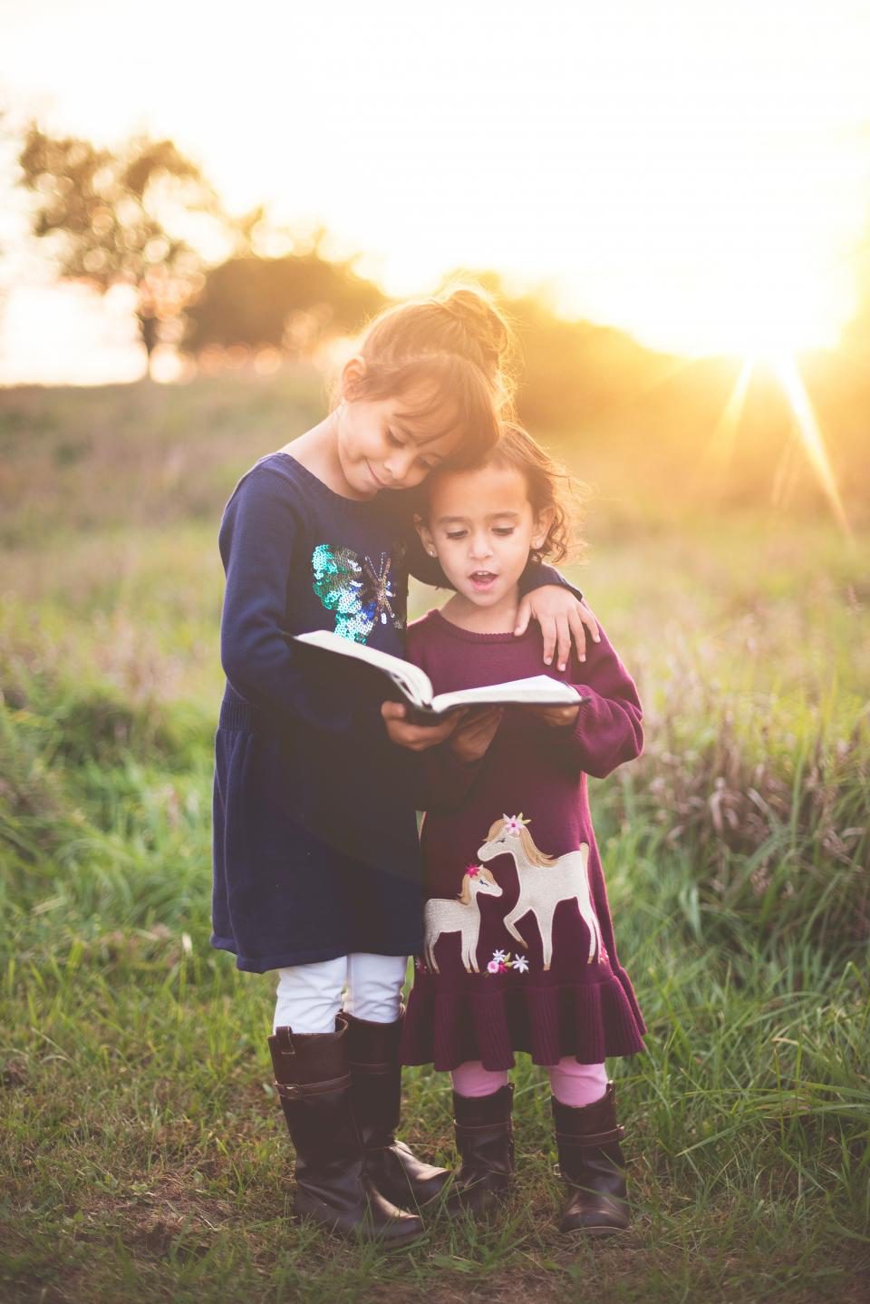 Twee kinderen kijken samen in een boek, buiten in de avondzon