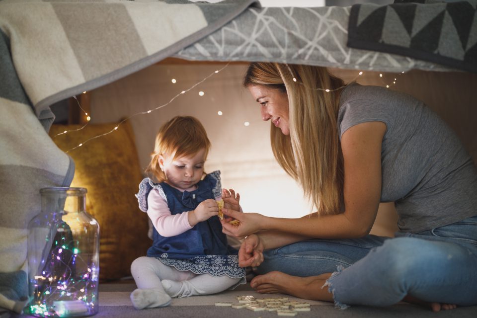Een peuter en een volwassene spelen samen in een gezellige speelhoek met lichtjes